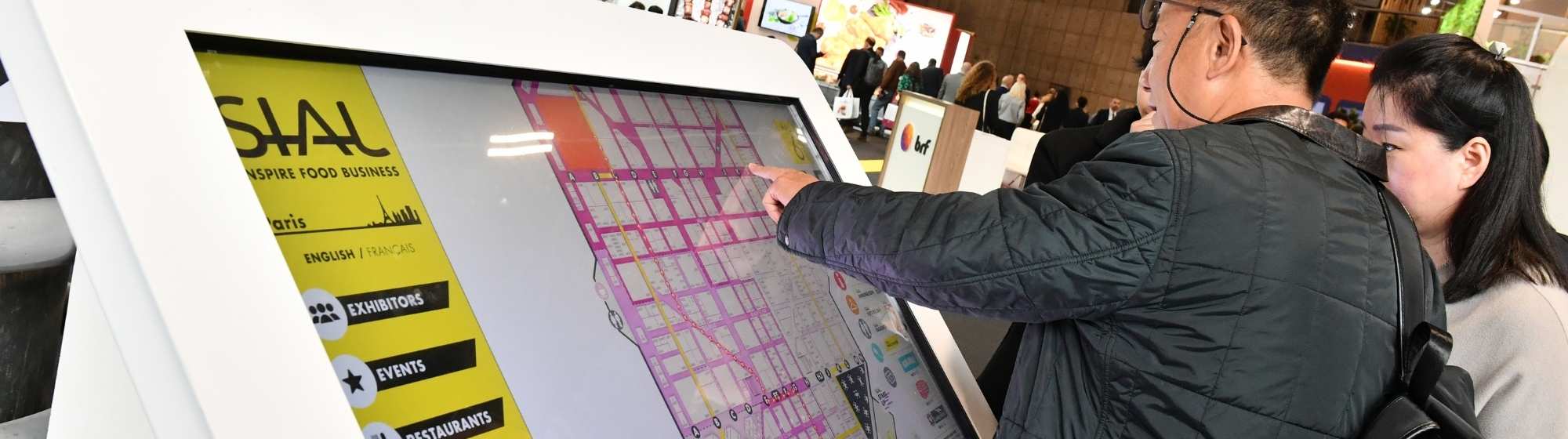 Two visitors use an interactive terminal to locate exhibitors at the SIAL Paris exhibition.