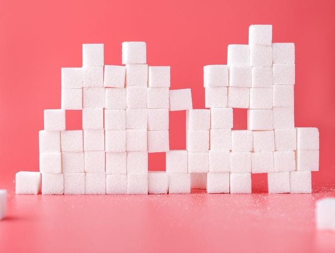 Stacked white sugar cubes forming a structure on a bright pink background.