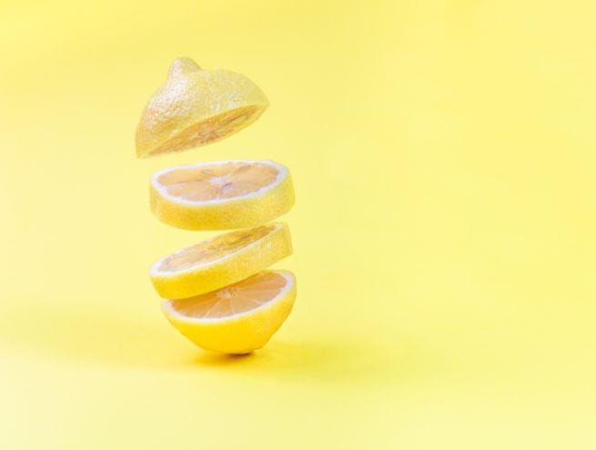 Un citron découpé en tranches flottantes sur un fond jaune uni.