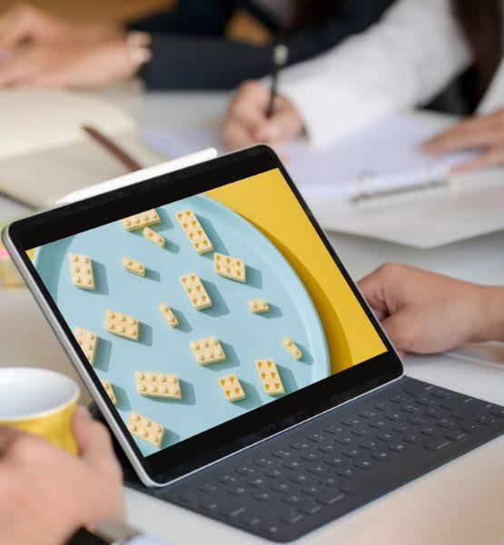 Meeting with a participant holding a tablet displaying building blocks on a blue plate, surrounded by others taking notes.